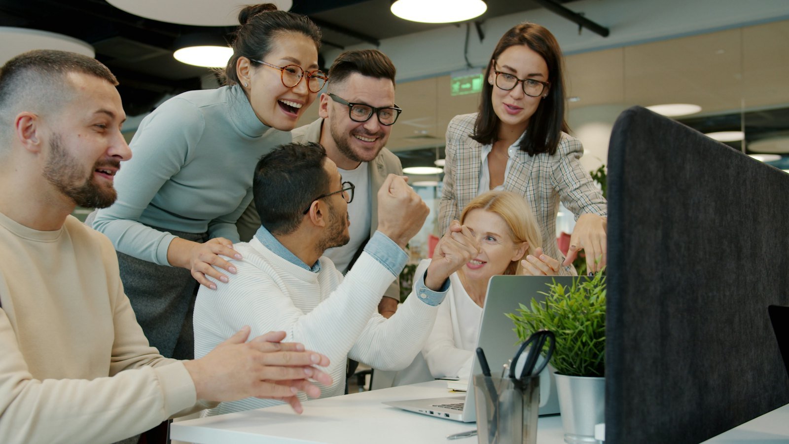 Equipo de trabajo celebrando una venta frente a la computadora
